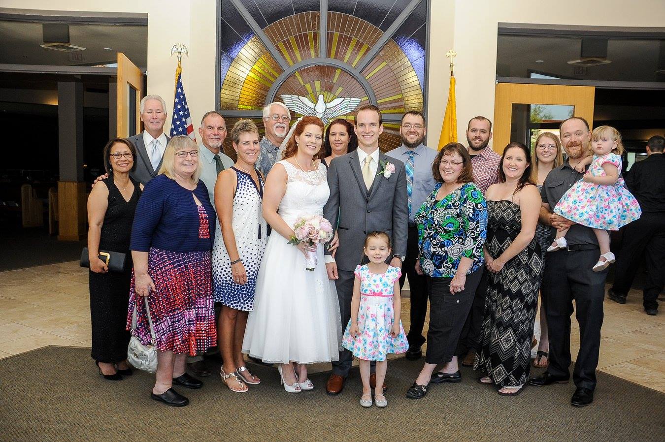 A young newly wedded couple poses for a photo with family in their wedding attire.