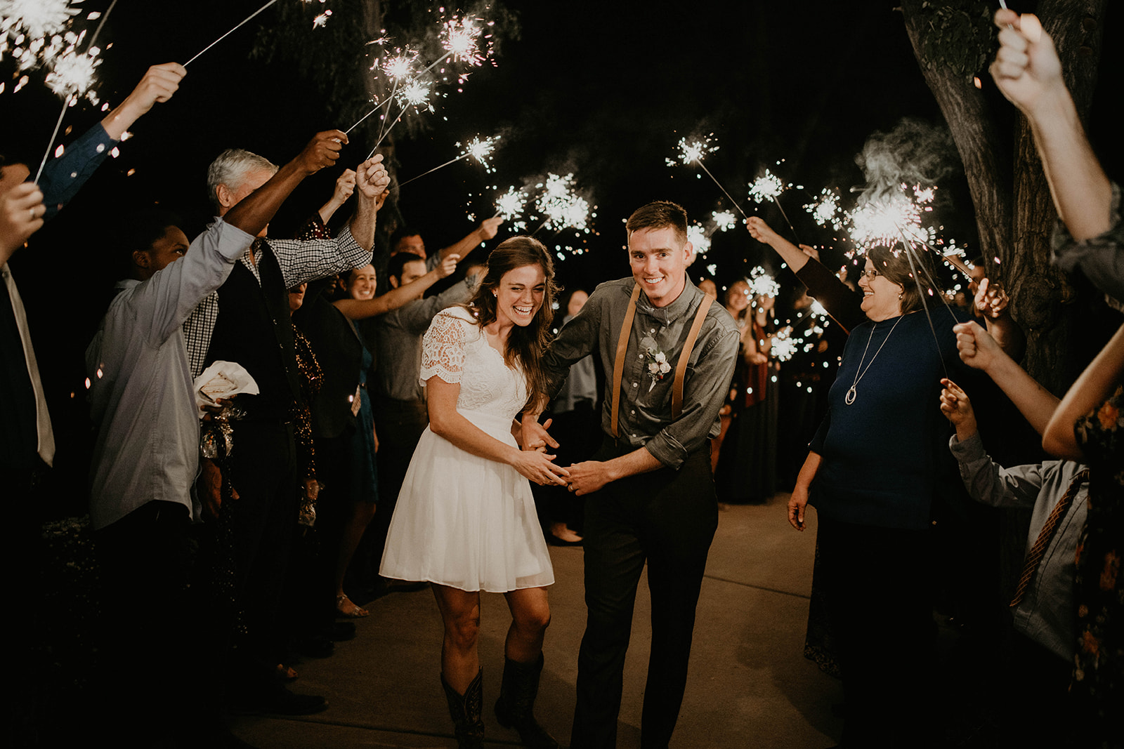 A young newlywed couple with sparklers says goodbye to guests at night, a beautiful end to the wedding day.